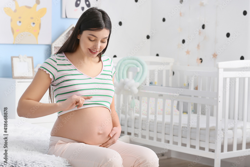 Young pregnant woman applying cream on her belly at home