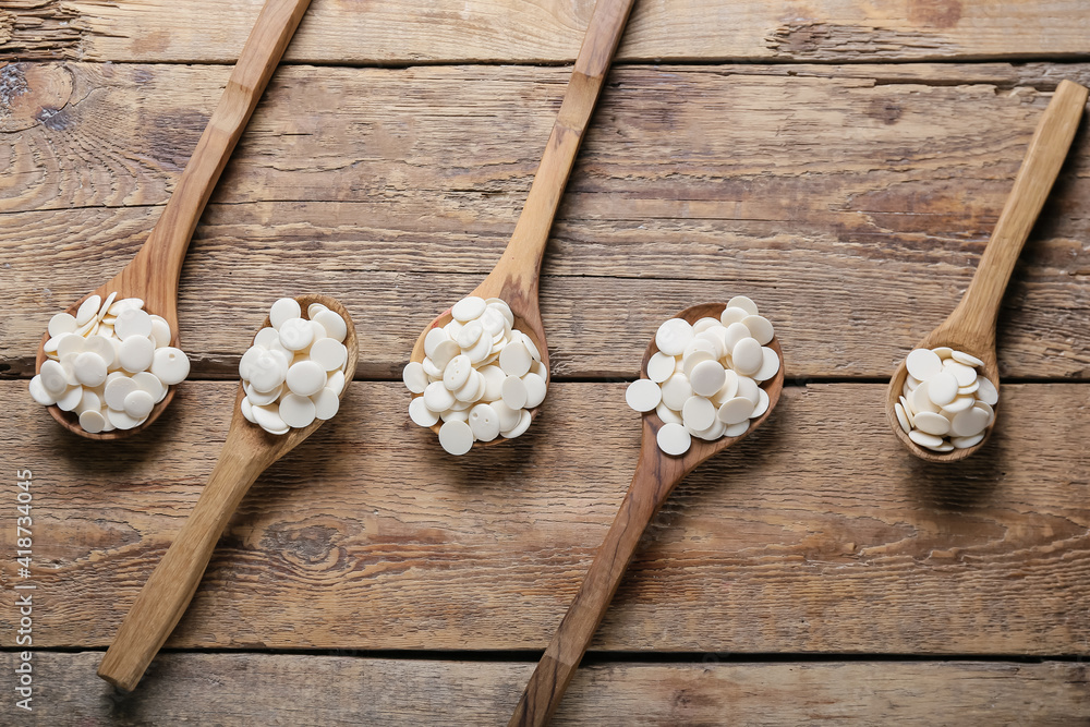 Spoons with chocolate drops on wooden background