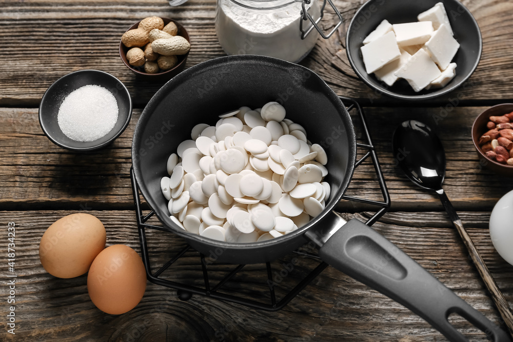 Saucepan with chocolate drops and ingredients for bakery on wooden background