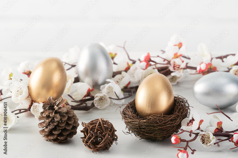 Close up of golden and silver Easter eggs in the nest with white plum flower.