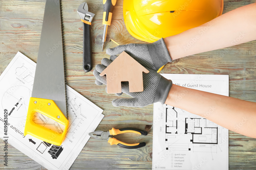 Female hands with figure of house and construction tools on wooden background