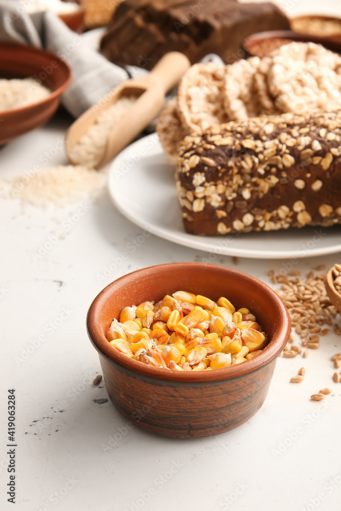 Bowl with corn grains and different products on light background, closeup