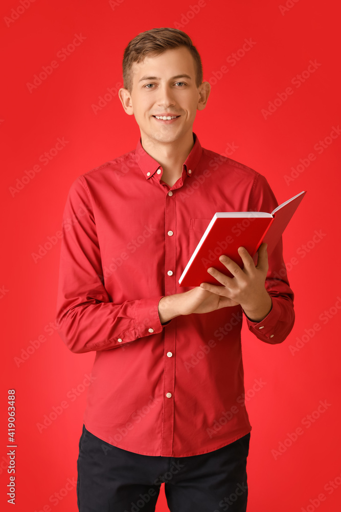 Young man with red book on color background