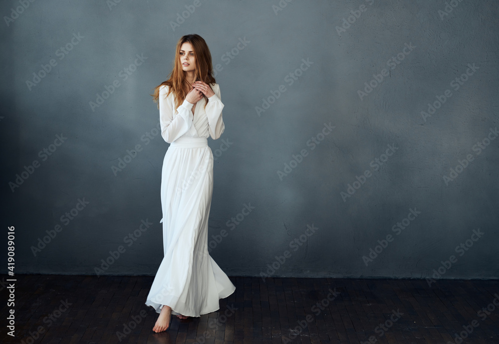 Red-haired Woman in a white dress in full growth on a gray background indoors