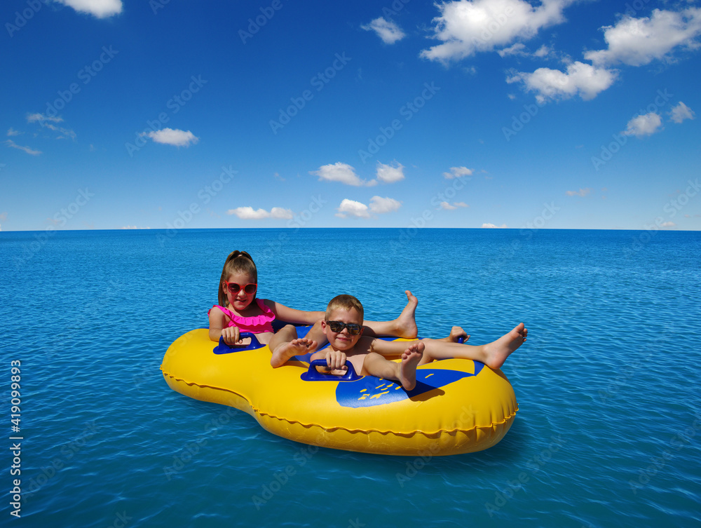 Boy and girl on inflatable float in blue sea water.