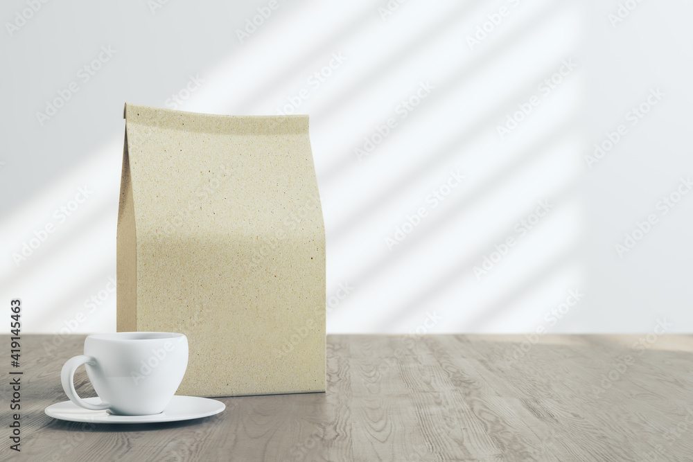 Blank craft paper tea package with white coffee mug on wooden table with light background. Mock up