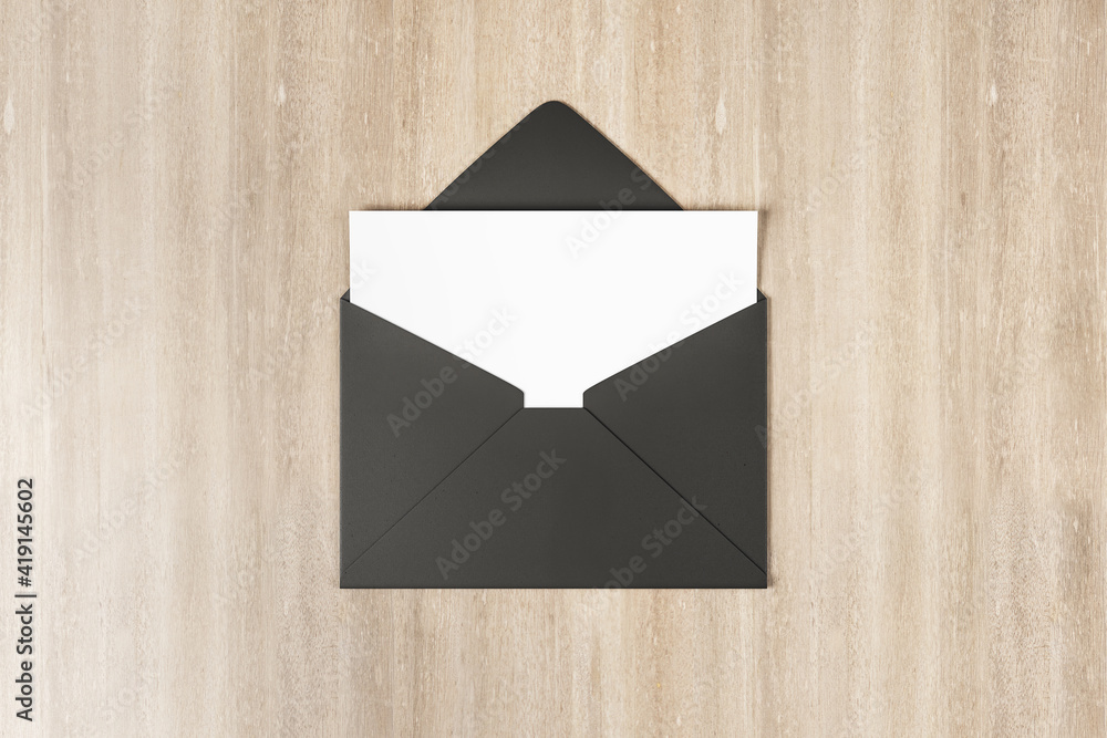 Blank white postal card in black envelope on wooden table. Mock up