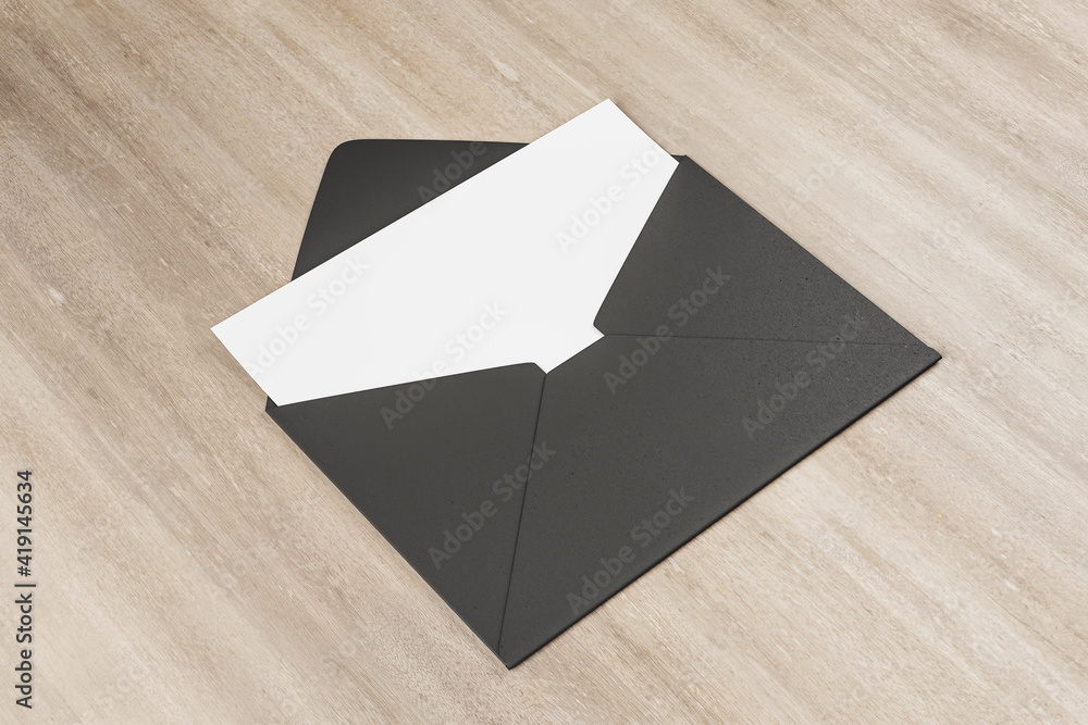 Black envelope with white blank card on wooden table. Mock up