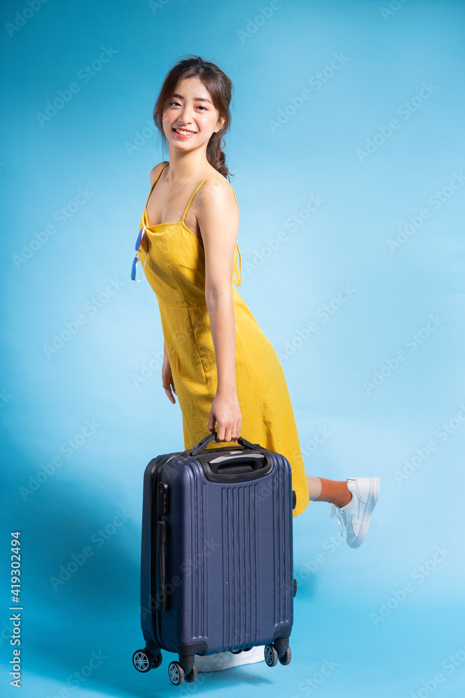 Young Asian woman holding suitcase on blue background, summer concept