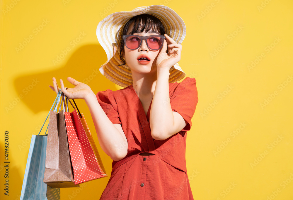 Young Asian businesswoman holding shopping bags posing on yellow background