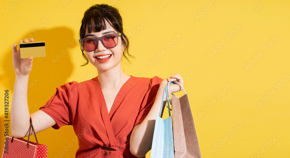 Young Asian businesswoman holding shopping bags posing on yellow background