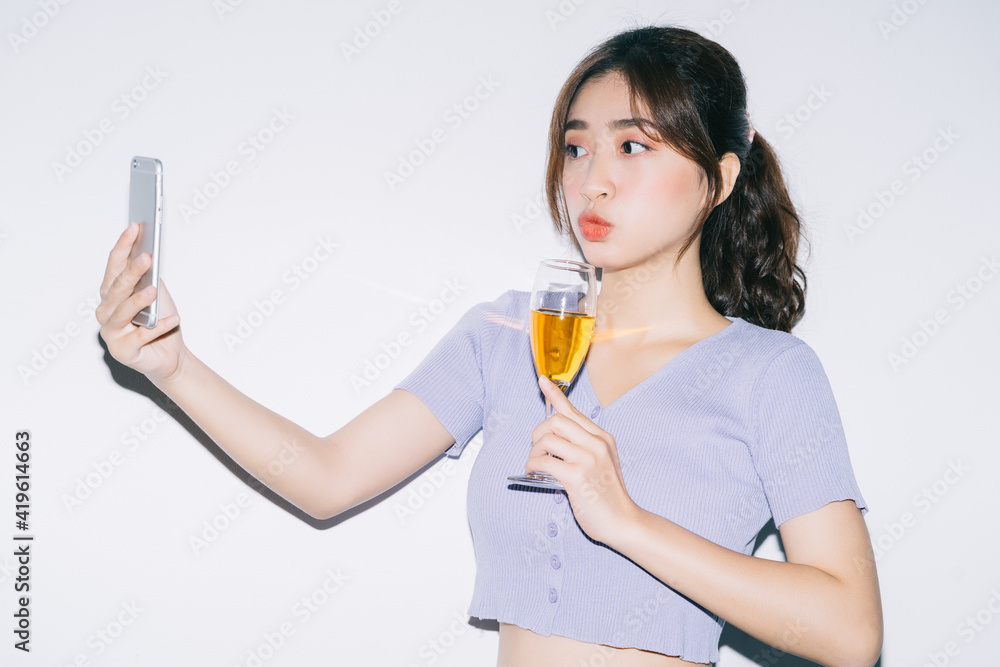 Young Asian woman drinking wine and using smartphone on white background