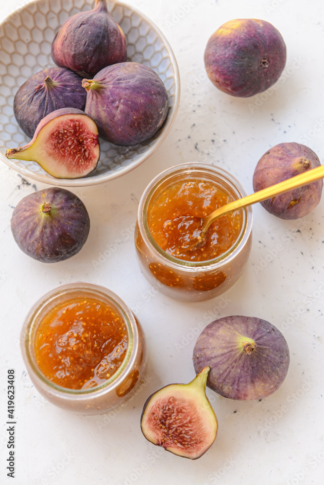 Glass jars with sweet fig jam on light background