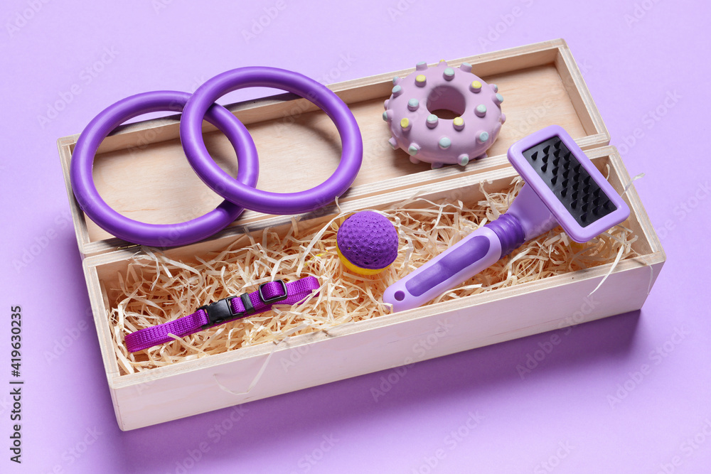 Box with different pet accessories on color background