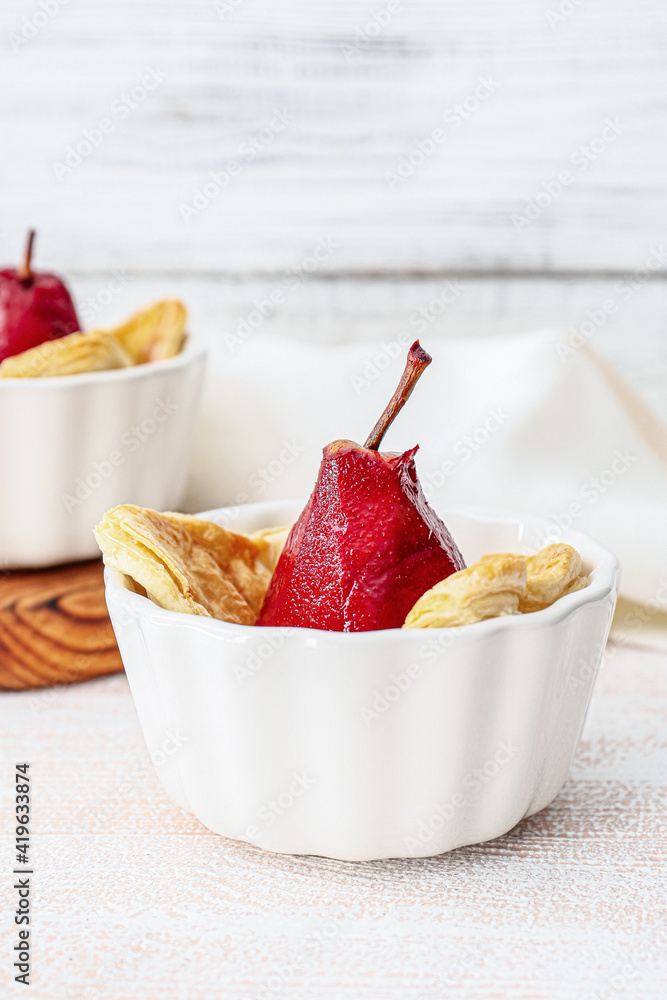 Dish of tasty poached pears in wine sauce on light wooden background