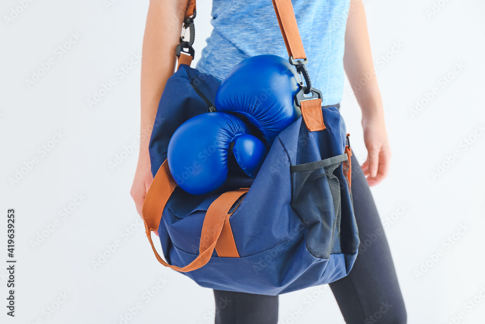 Young woman with sports bag and boxing gloves on white background