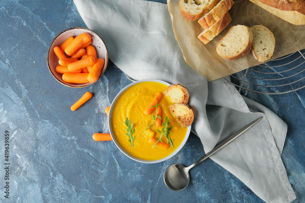 Bowl of carrot cream soup on color background