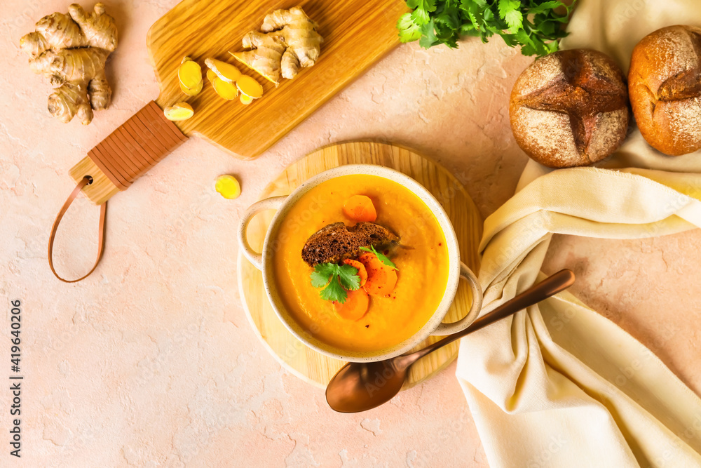 Cooking pot of fresh carrot cream soup on color background