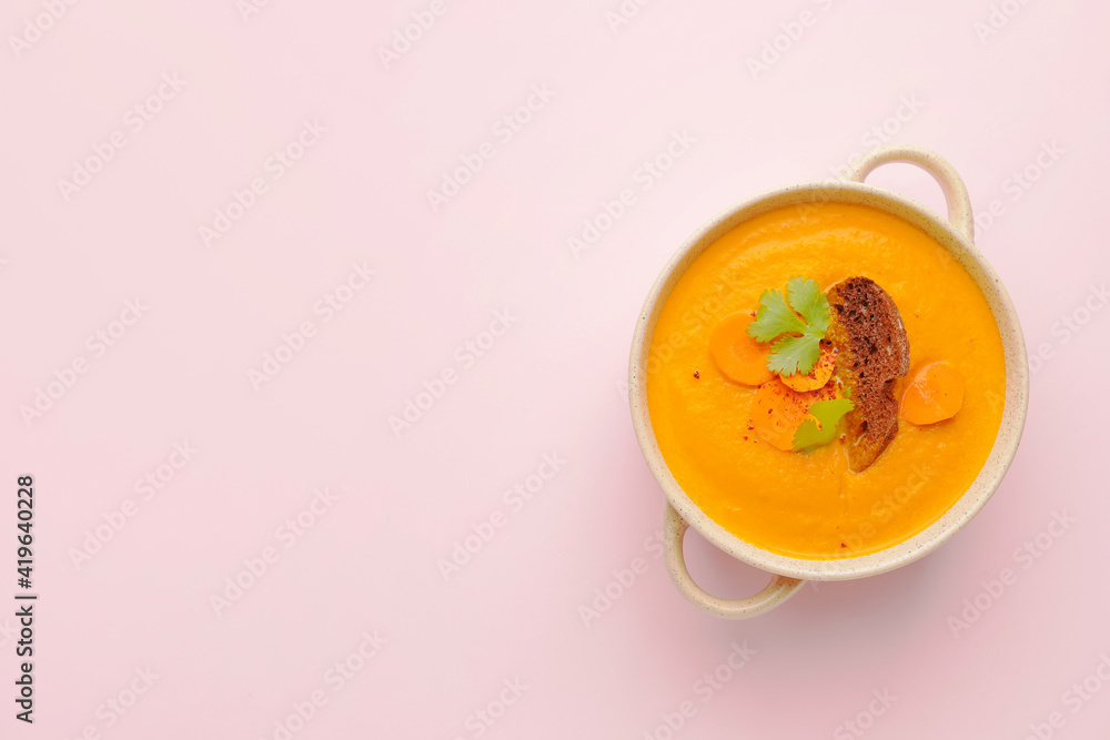 Cooking pot of fresh carrot cream soup on color background