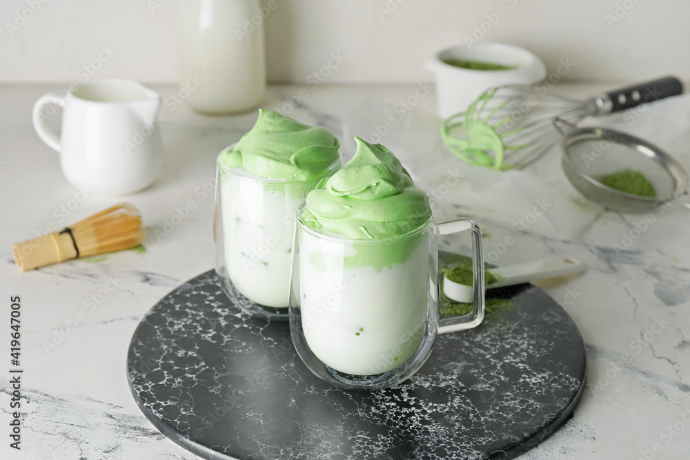 Board with cups of tasty dalgona matcha latte on light background