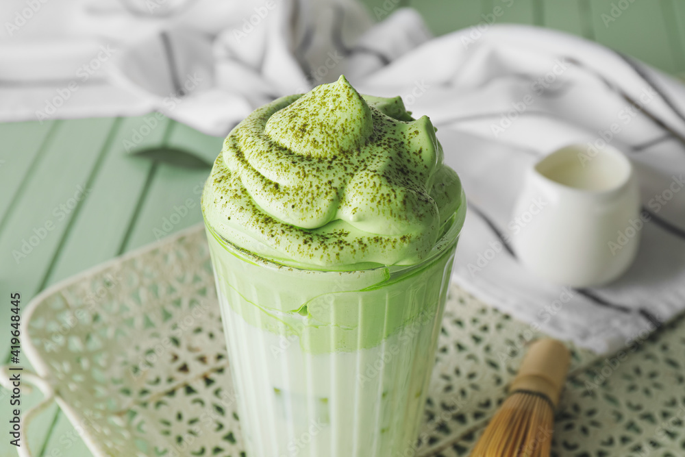 Glass of tasty dalgona matcha latte on color wooden background, closeup