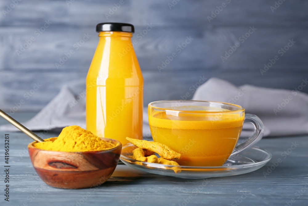 Cup and bottle of healthy turmeric drink on color wooden background