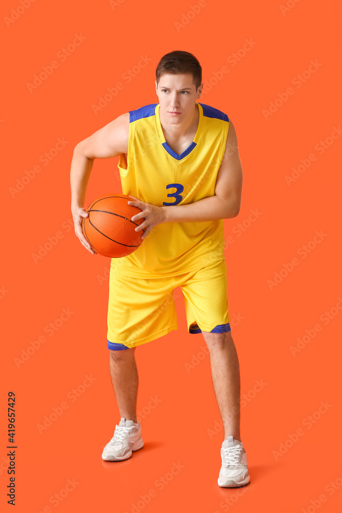 Handsome young man playing basketball on color background