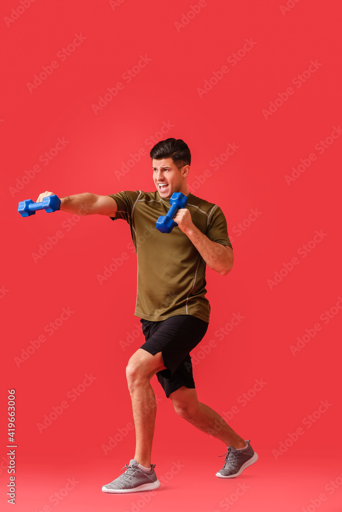 Sporty young man training with dumbbells on color background