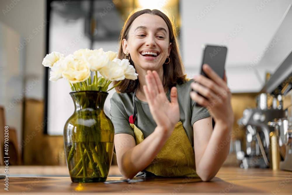 Young woman speaks on phone while staying near a bouquet of fresh tulips in stylish kitchen. Greets 