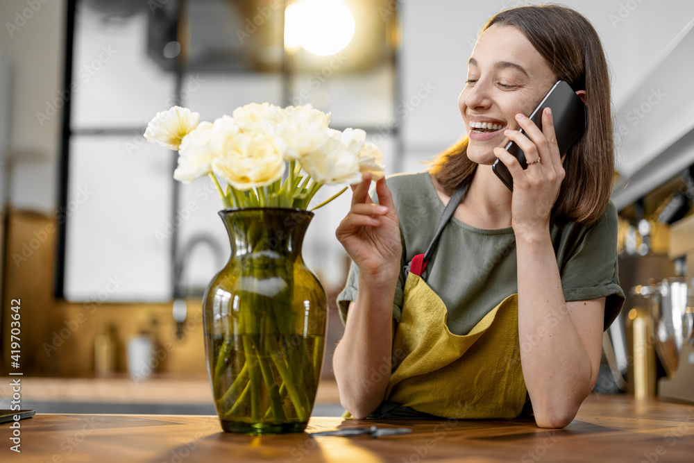 Young woman speaks on phone while staying near a bouquet of fresh tulips in stylish kitchen. Gratefu