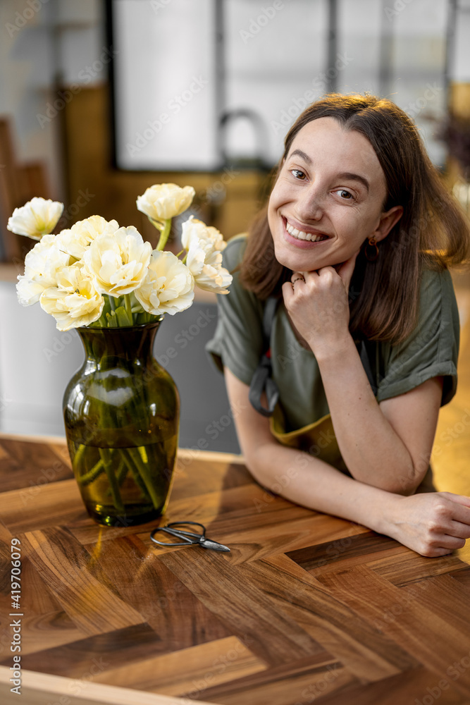 Portrait of young housewife with a bouquet of fresh tulips on stylish interior of kitchen. A vase wi