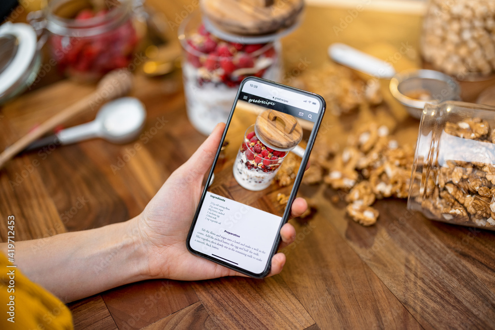 Digital recipe of healthy breakfast with granola on the phone screen on wooden table top in kitchen 