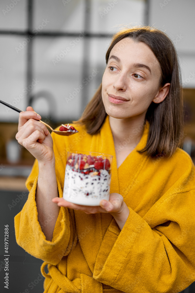 穿着黄色浴袍的年轻女子享用健康的谷物早餐，碗里有酸奶和浆果o