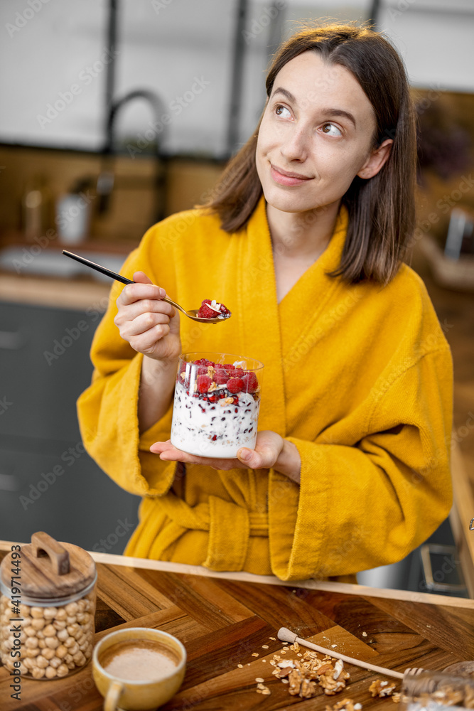 穿着黄色浴袍的年轻女子享用健康的谷物早餐，碗里有酸奶和浆果o