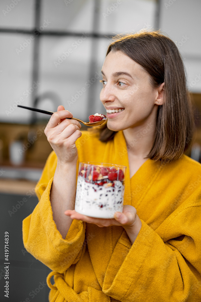 穿着黄色浴袍的年轻女子享用健康的谷物早餐，碗里有酸奶和浆果o