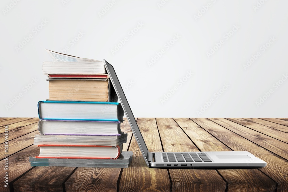 Stack of books with modern laptop on table