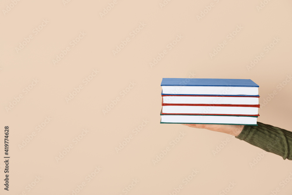 Female hand with stack of books against color background