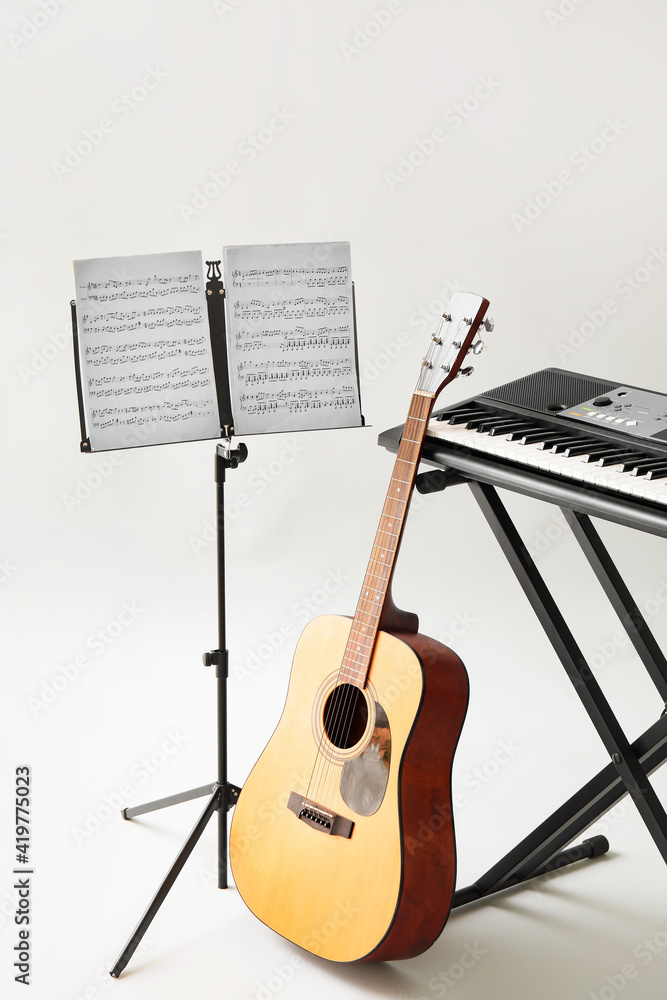 Note stand with music sheets, acoustic guitar and synthesizer on light background