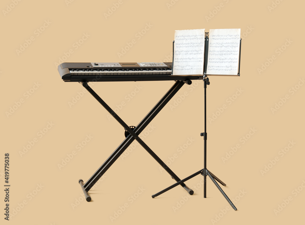 Note stand with music sheets and synthesizer on color background