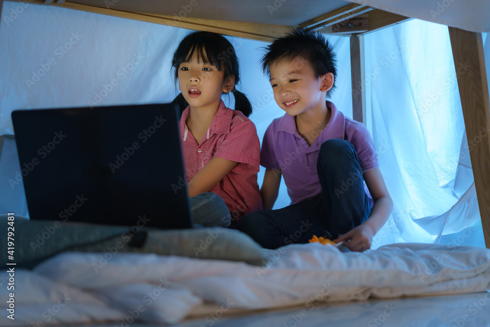 Asian boy child and his sister to make a camp to play imaginatively watching a film on laptop in the