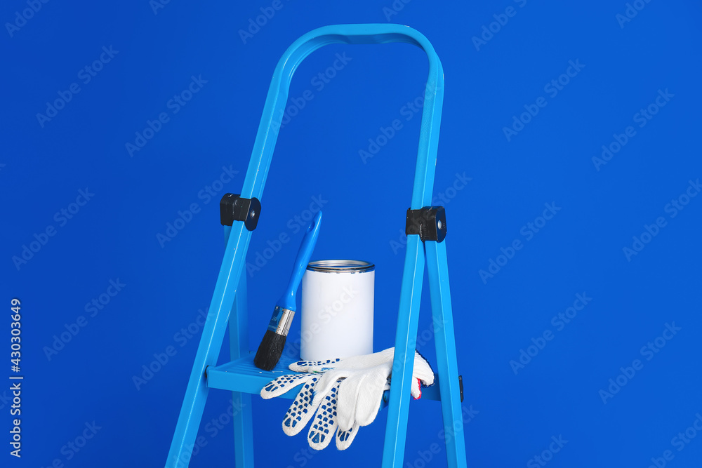 Ladder with can of paint, brush and gloves near color wall