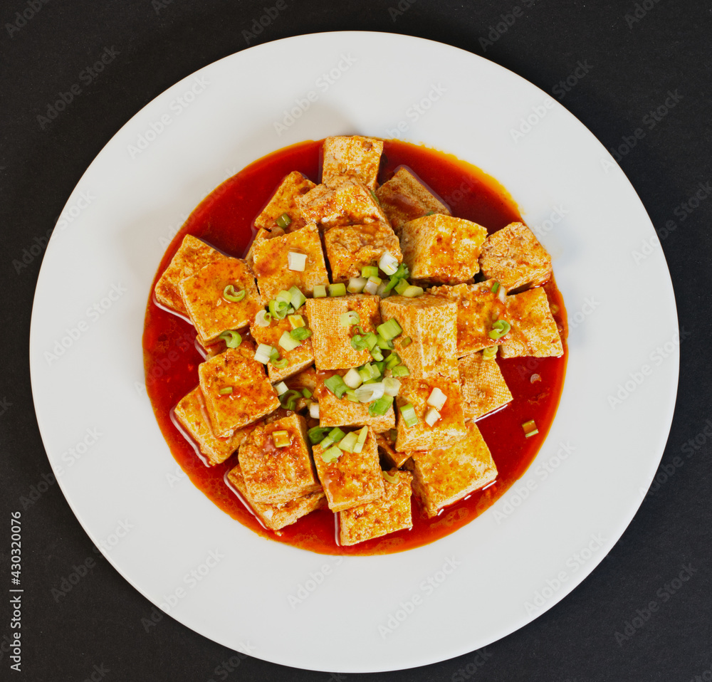 Spicy Tofu with red sauce in a white dish, black background, top view