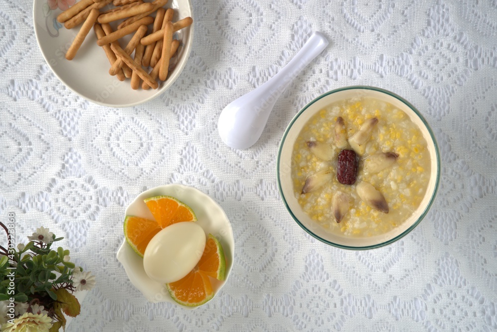 Healthy and nutritious lily red dates porridge, eggs, finger biscuits, oranges, spoon. Top view, whi