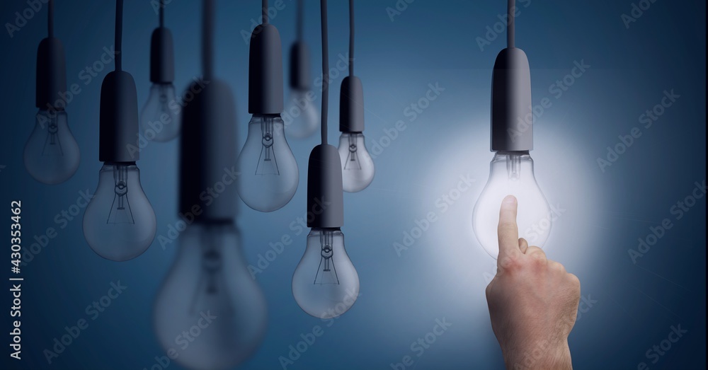 Composition of multiple light bulbs hanging with finger touching lit light bulb on blue background