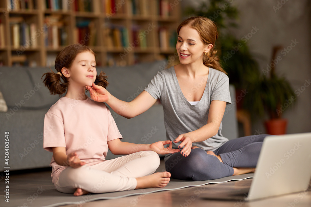 Young happy mother teaching child meditation techniques while having online yoga class