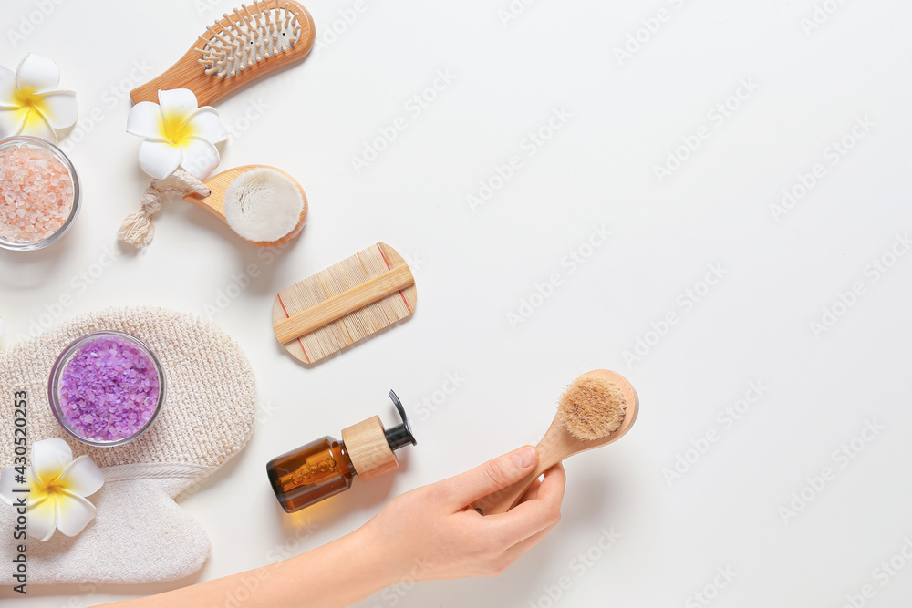 Female hand with massage brush and bath supplies on white background