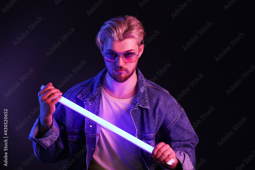 Toned portrait of handsome young man with neon lamp on dark background