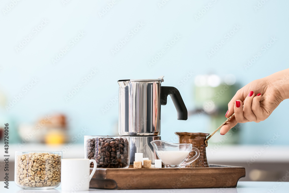 Female hand with coffee pot, cup of espresso and beans on table in kitchen