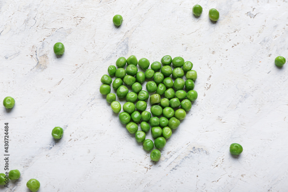 Heart made of fresh green peas on light background