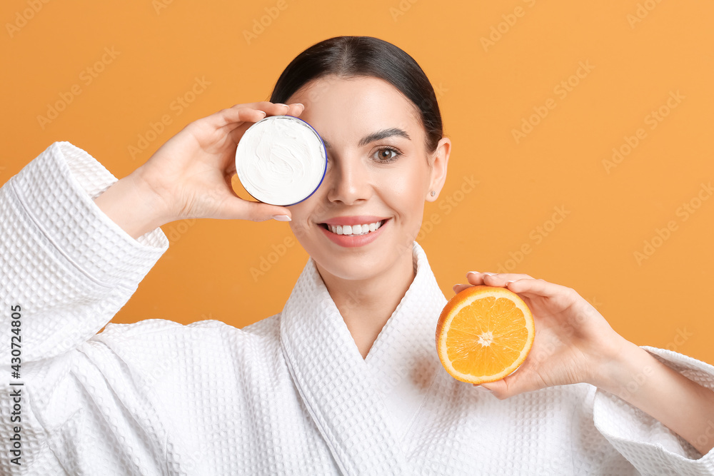 Beautiful young woman with orange and facial cream on color background